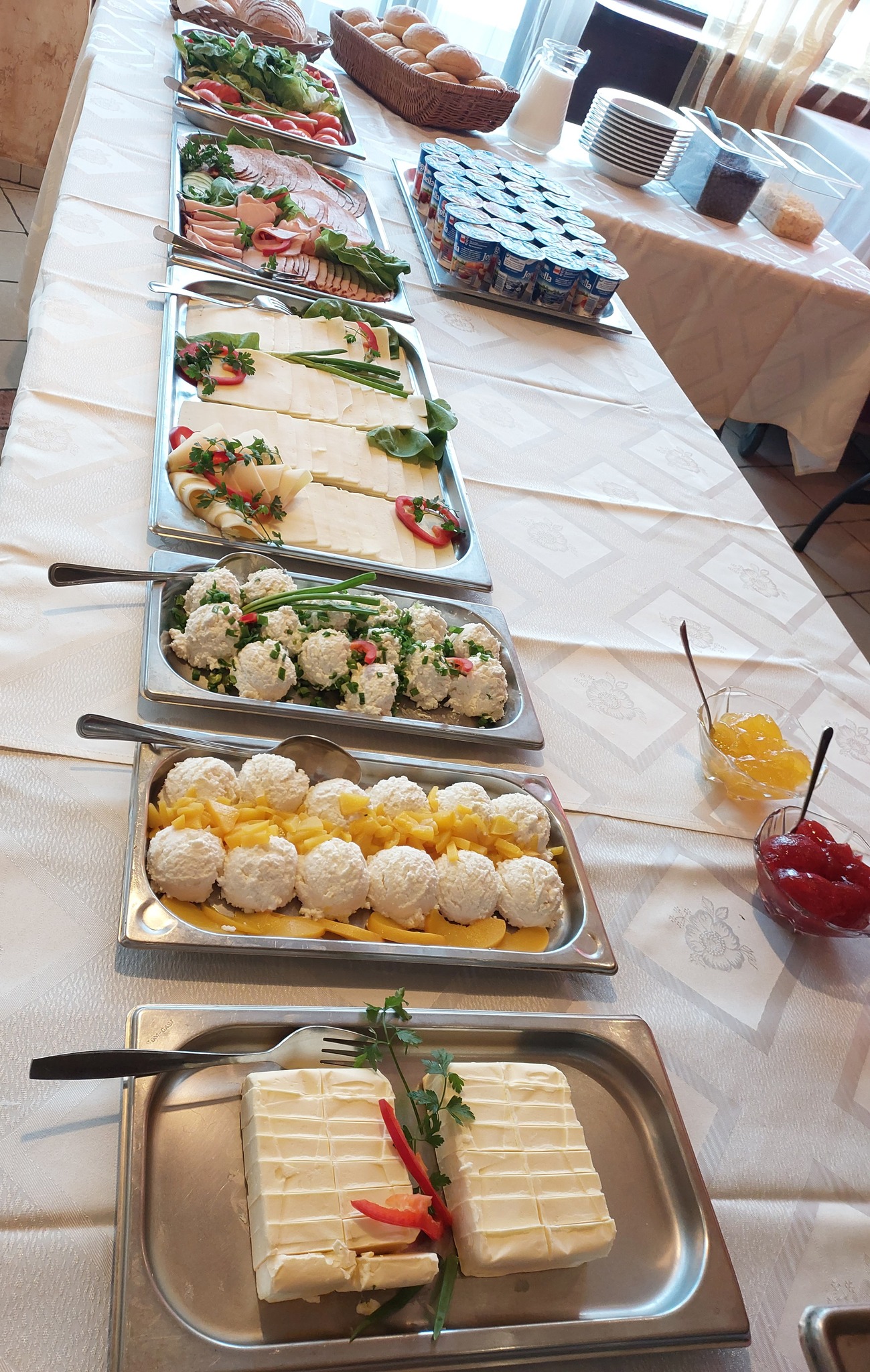 Breakfast buffet - cream cheese, cottage cheese with sweet and chives, cold cuts, tomatoes, peppers, bread, butter, yogurt, jams, cereals with milk.