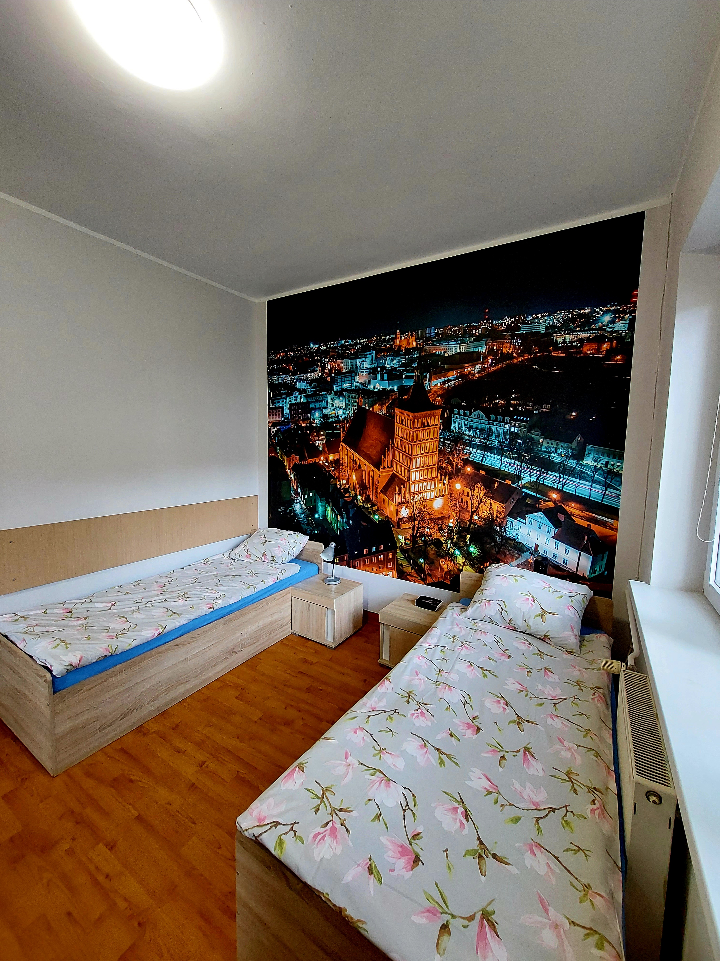 Ein Zweibettzimmer mit Bad im Objekt Nr. 1 Kosciuszko. Die Tapete im Hintergrund an der Wand zeigt Olsztyn aus der Vogelperspektive.  
